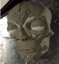 The image shows an anatomical model of a human head made of clay over a white base. Several facial muscles are roughly represented, including the frontalis, orbicularis oculi, zygomatic muscles, and orbicularis oris. This type of model is commonly used in anatomy or sculpture classes to study the arrangement of facial muscles.
